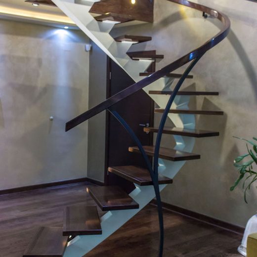 Zakrivljeno elipsasto stepenište sa belom nosećom gredom, drvenim gazištima i elegantnom zakrivljenom tamnom ogradom