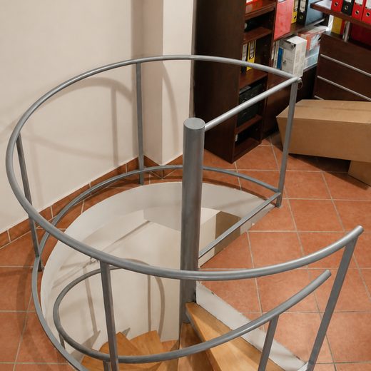 Pogled iz gornjeg ugla na sivu konstrukciju spiralnih stepenica sa drvenim gazištima i polukružnom ogradom galerije