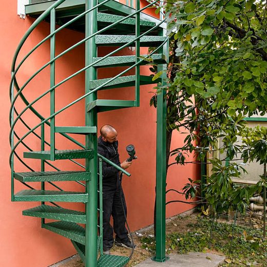 Zeleno spoljno spiralno metalno stepenište tokom postupka farbanja i zaštite u dvorištu