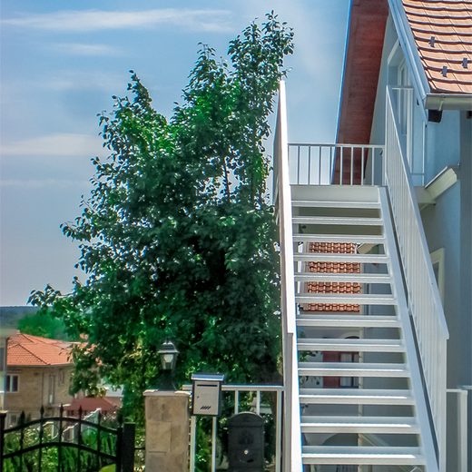 Pogled odozdo na spoljno čelično stepenište sa belom zaštitnom ogradom i protivkliznim gazištima